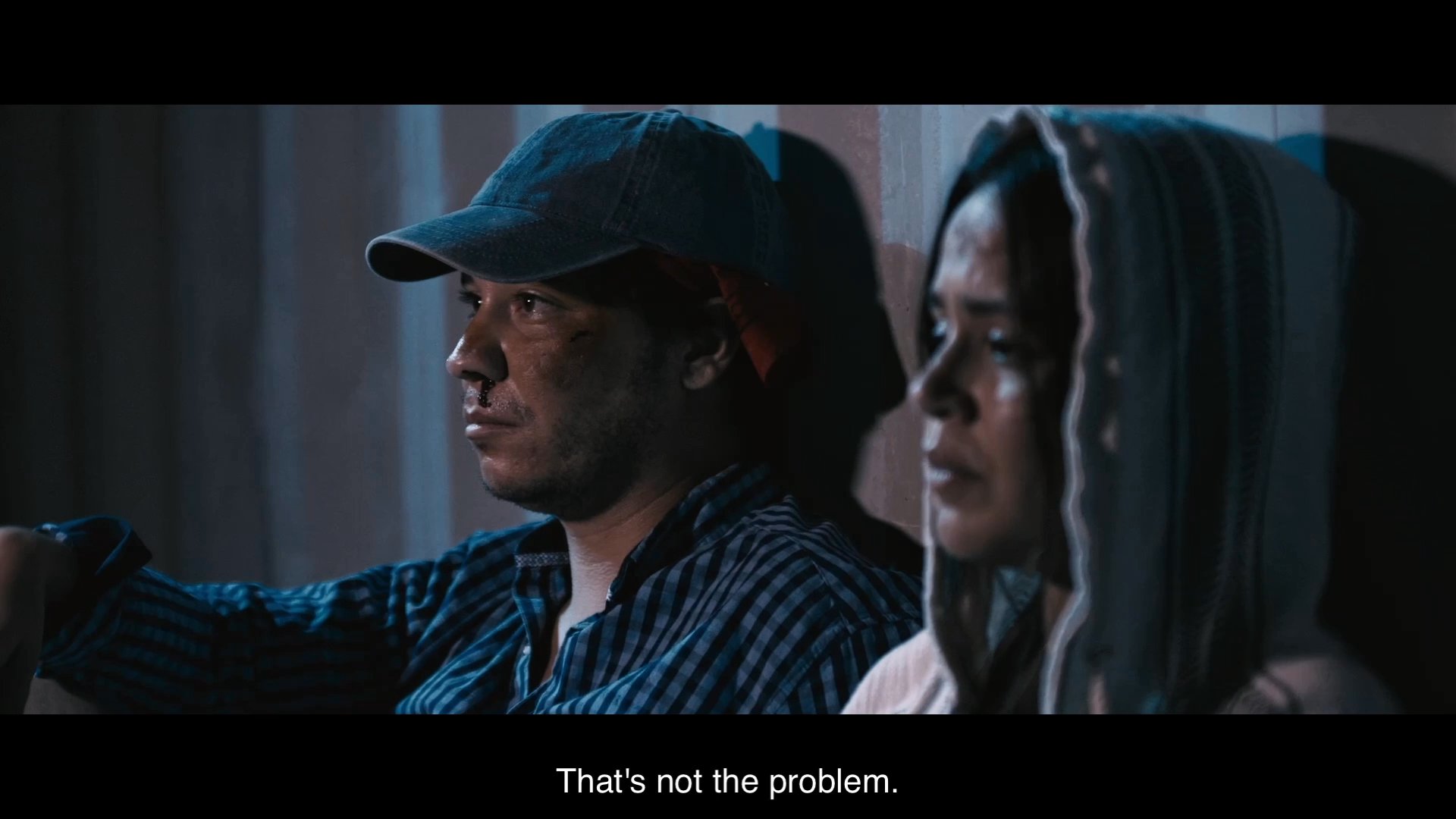 Two individuals engage in a somber, intimate conversation characterized by unresolved conflict and personal disappointment. The scene focuses on their tense emotional exchange in a dimly lit environment.