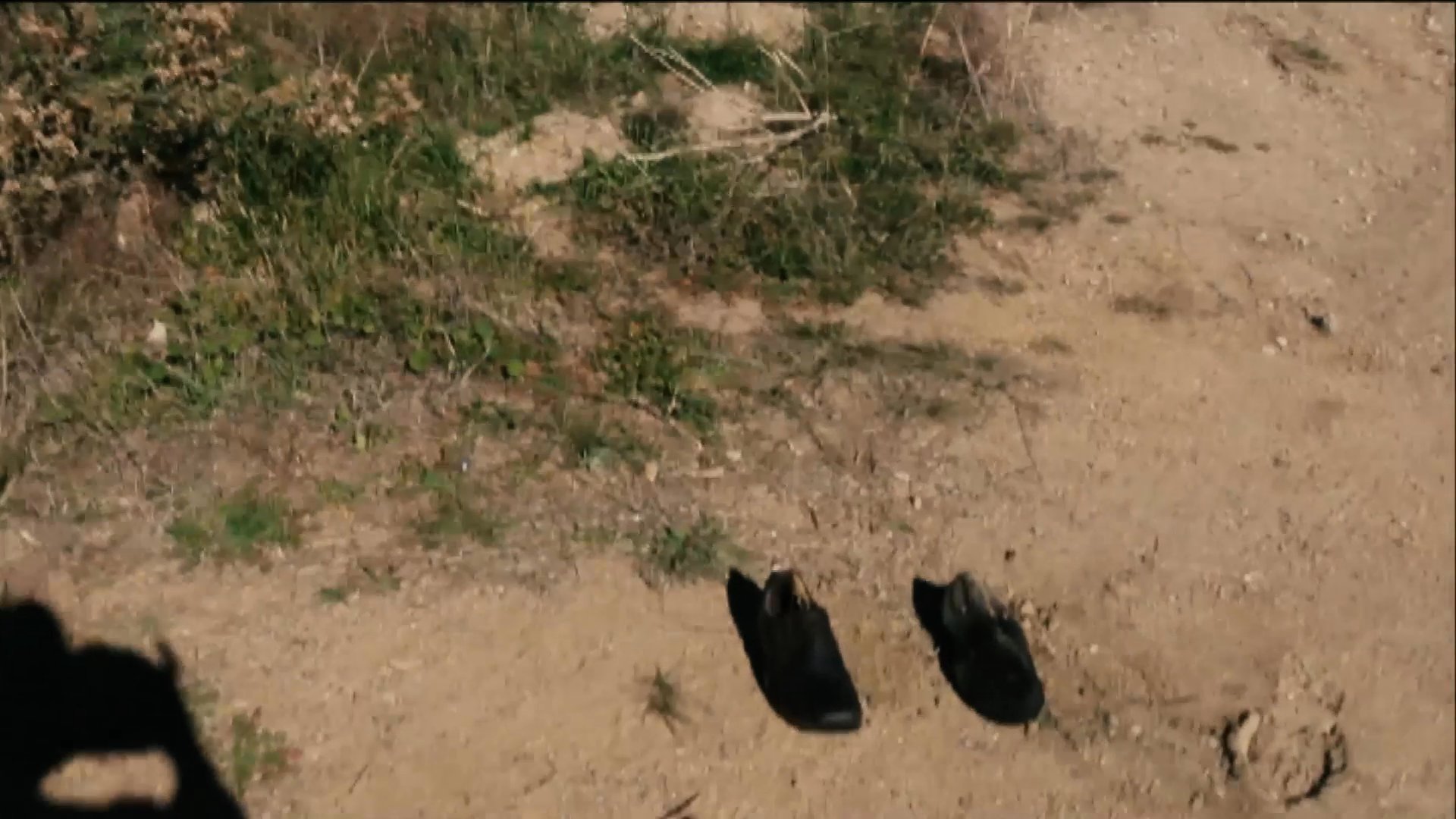 A presenter stands in an outdoor field before a sudden pyrotechnic effect obscures the scene. The smoke dissipates to reveal a pair of shoes left on the ground, serving as the focal point for the remaining sequence.