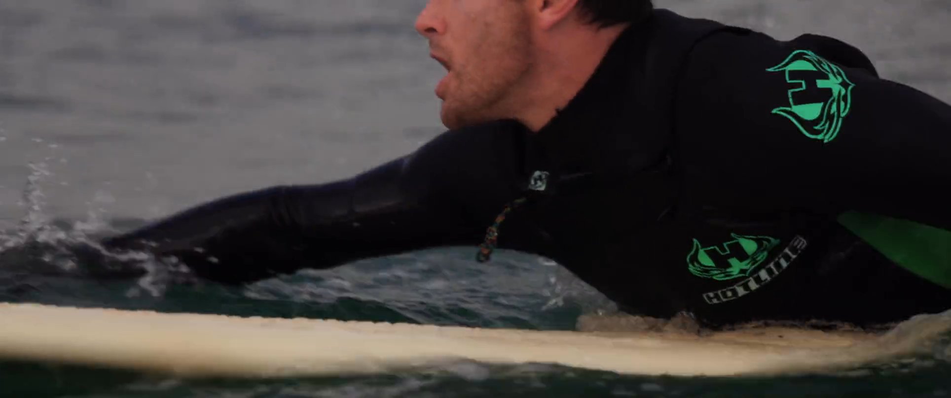 A focused surfer in a wetsuit maneuvers their board through choppy ocean waters, preparing to catch an approaching wave.