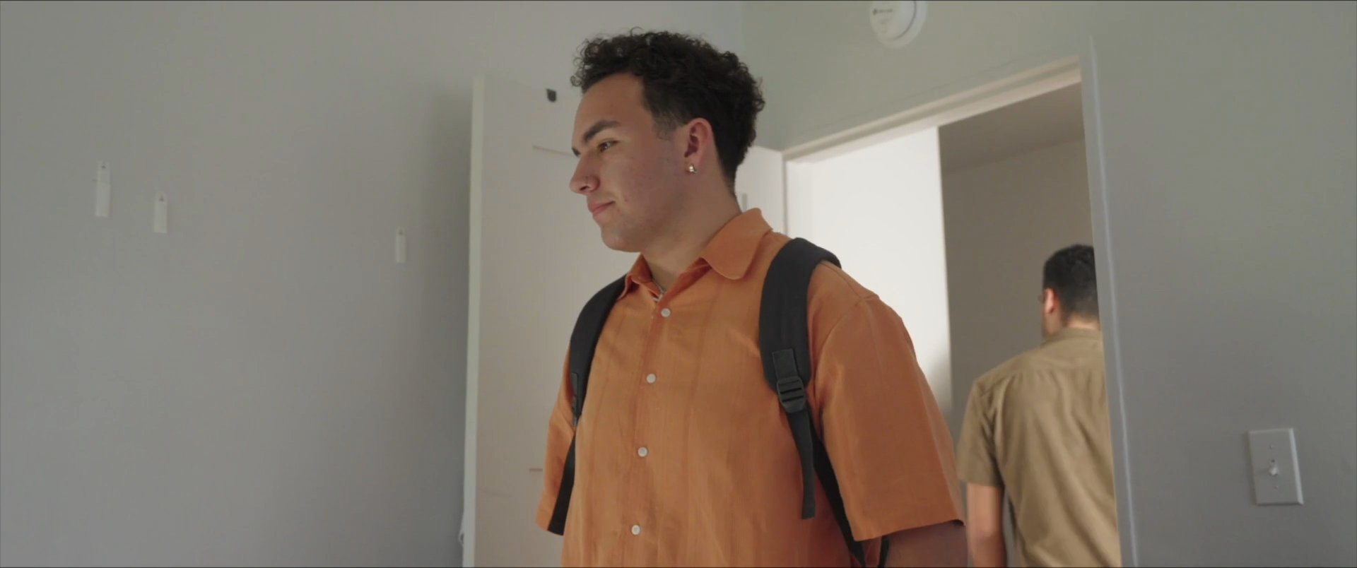 Two students share a final conversation in a dorm room before one departs for a theatre rehearsal. The scene transitions to a poster advertising a stage production, followed by a snippet of the performance.