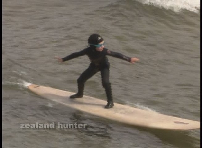 A young surfer practices balance and technique on a surfboard while receiving guidance in the ocean. The child maintains focus as an instructor provides support to navigate the gentle waves.