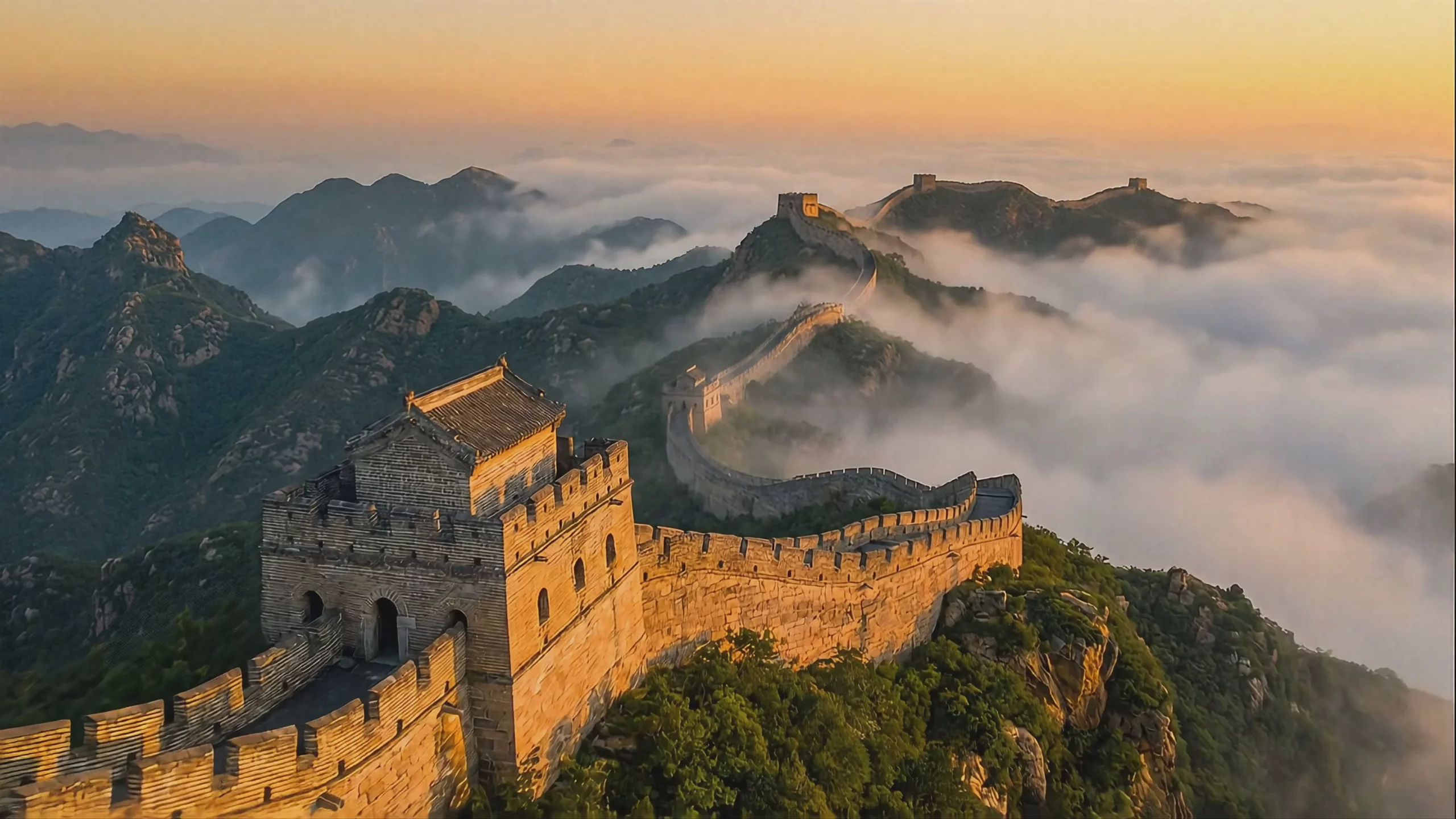 A wide-angle aerial view of the Great Wall of China snaking across green mountain ridges partially covered by a thick blanket of low clouds. The scene is illuminated by warm golden hour sunlight, highlighting a stone watchtower in the foreground. This 1920x1080 video frame was generated using the Veo 3 model.