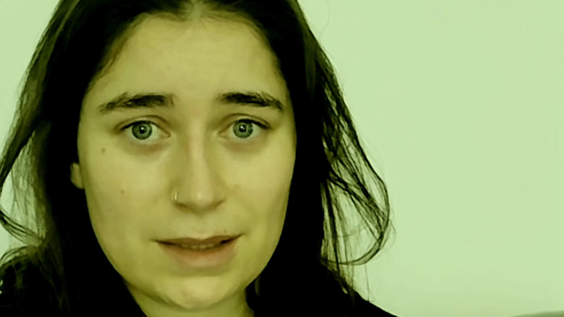 A woman maintains direct eye contact while speaking to the camera against a neutral background. Her nuanced facial expressions indicate an engaged and articulate delivery.