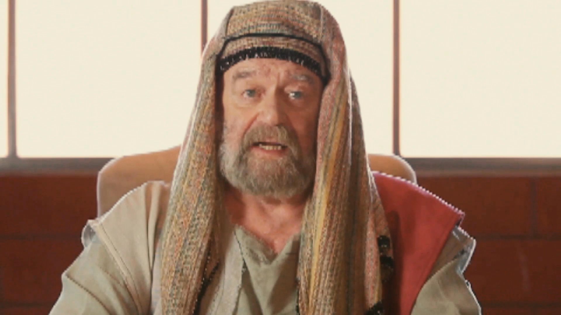 A man dressed in period-accurate historical robes engages in a formal discussion with two individuals within a modern office setting. The interaction centers on a professional dialogue held across a boardroom table.