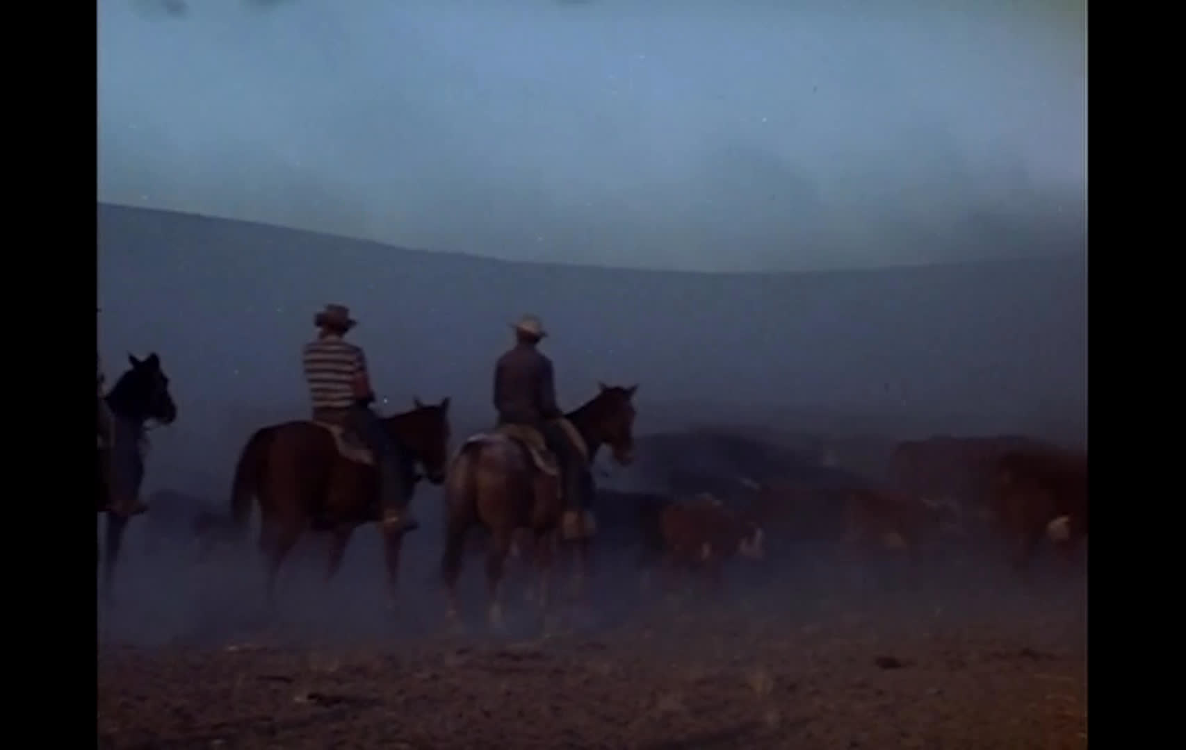 A lone rider crosses a dim, fenced landscape before cowboys on horseback move cattle across a dusty open range. The riders recede into the haze, evoking the struggle over land and grazing rights described in the narration.