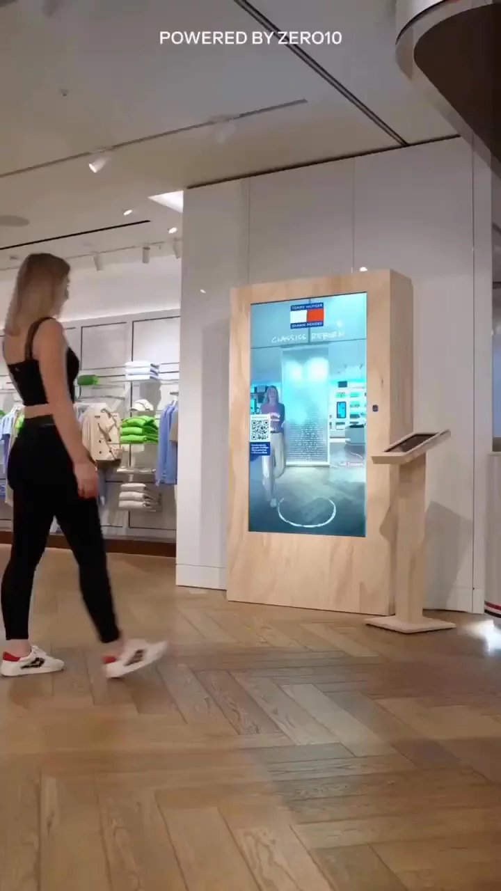  A woman stands confidently in front of a large screen in Tommy Hilfiger Store, engaging try on clothes with the displayed AR content.