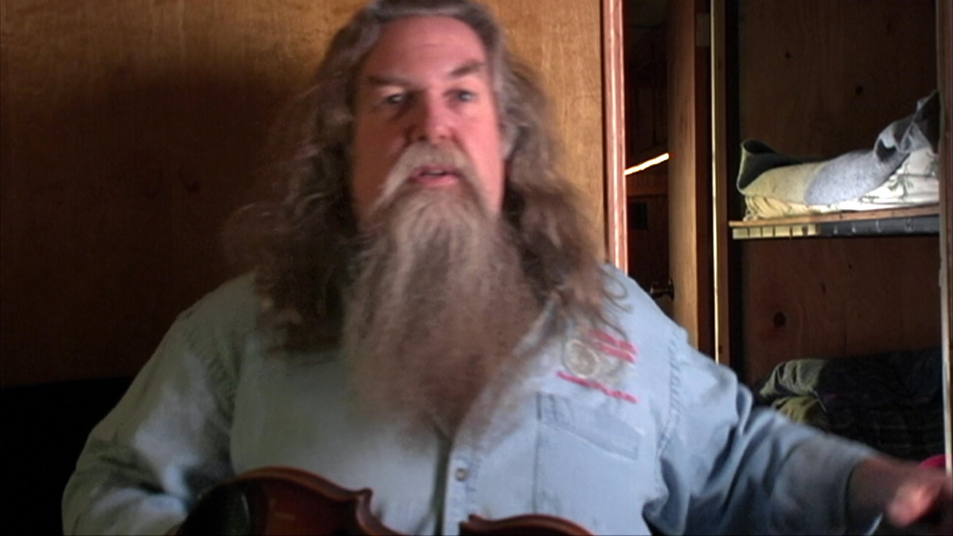 A man with a long beard uses expressive hand gestures to tell a story while sitting indoors. He conveys emotion and emphasis through varied arm movements and facial expressions.
