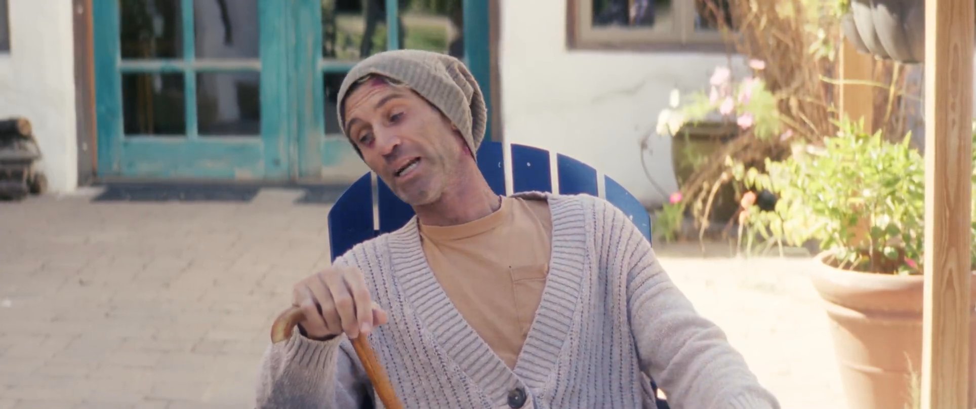 Two men engage in a supportive conversation on an outdoor patio, culminating in one man using a cane to stand up with his friend's encouragement.