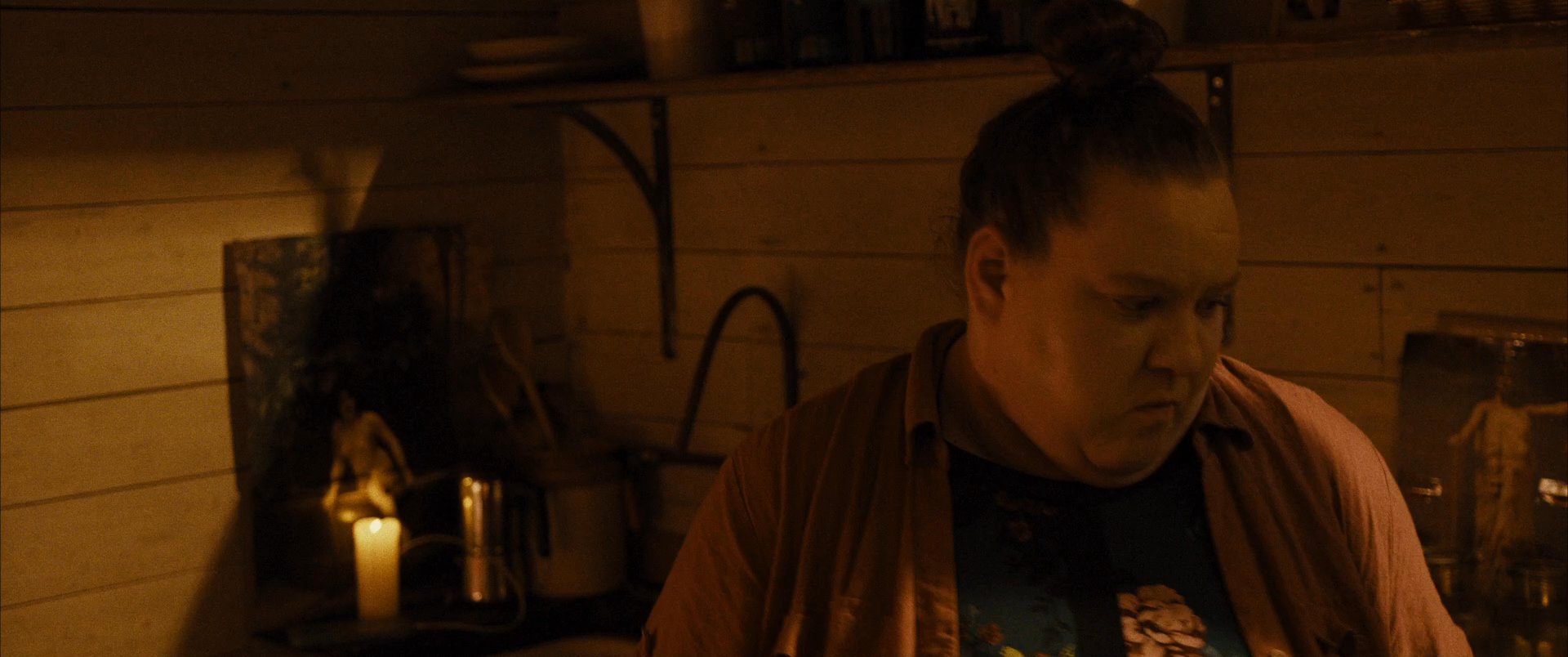 Two individuals engage in a conversation within a dimly lit, rustic cabin environment illuminated by lanterns and candles.