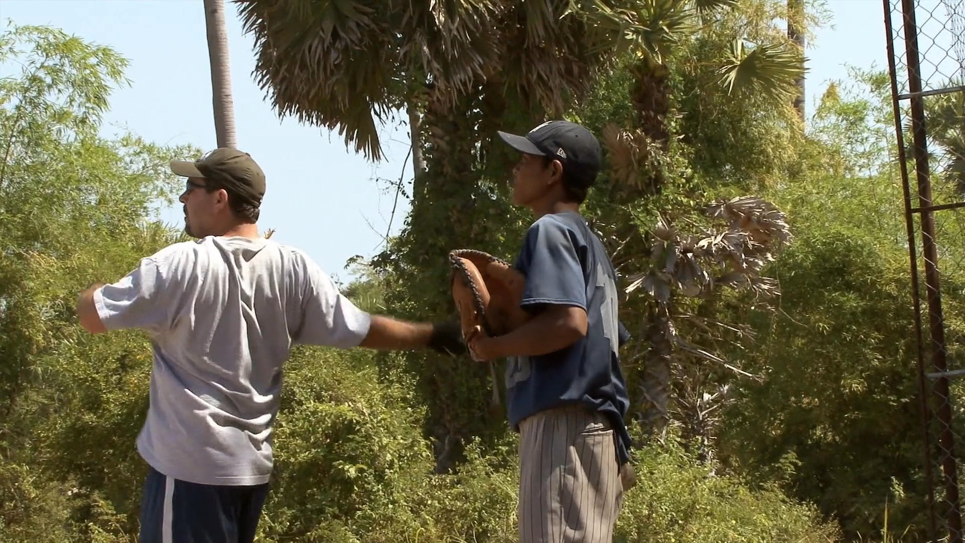 Instructors guide a group of players through baseball fundamentals, including fielding techniques and batting practice on an outdoor field.