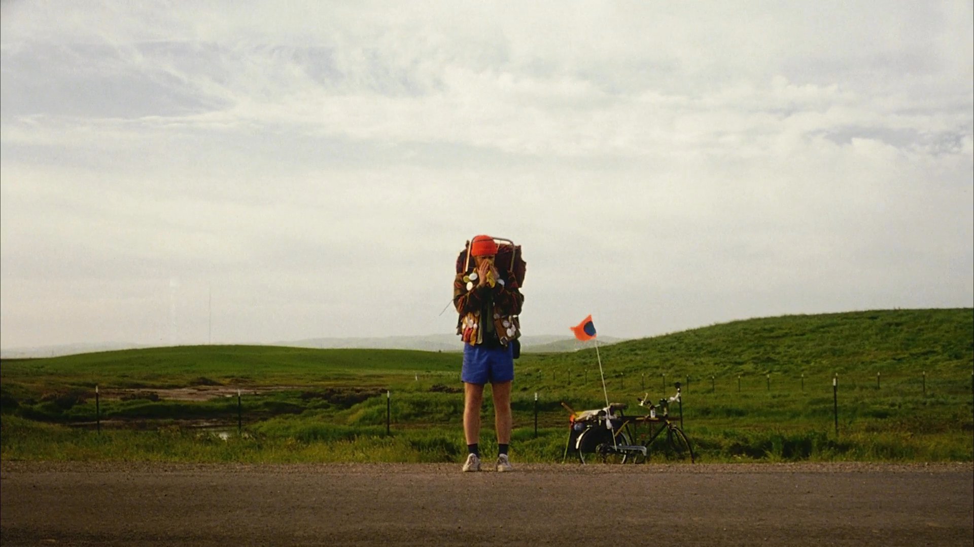 A distressed driver experiences an emotional breakdown while traveling along an open road, while a lone backpacker waits on the roadside.