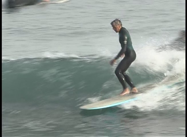 A man in a wetsuit skillfully rides a surfboard across the face of an ocean wave. He maintains balance and maneuverability while navigating the shifting water surface.