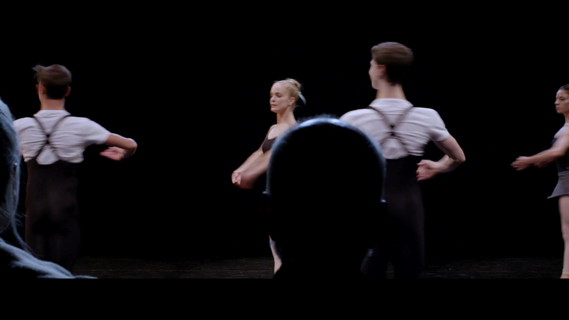 Dancers perform choreography on a stage while a panel of judges observes and evaluates their technique. The session focuses on professional dance assessment in a formal setting.