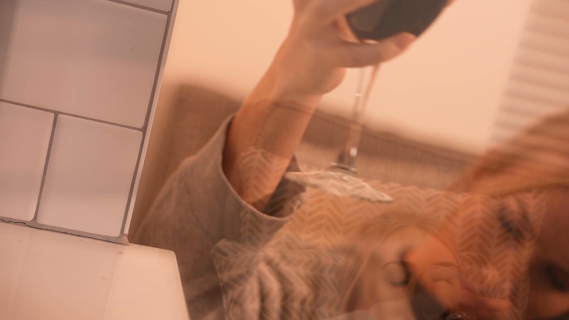 A woman relaxes in a kitchen environment, periodically drinking from a glass of red wine. The sequence captures a quiet moment of downtime in a residential setting.