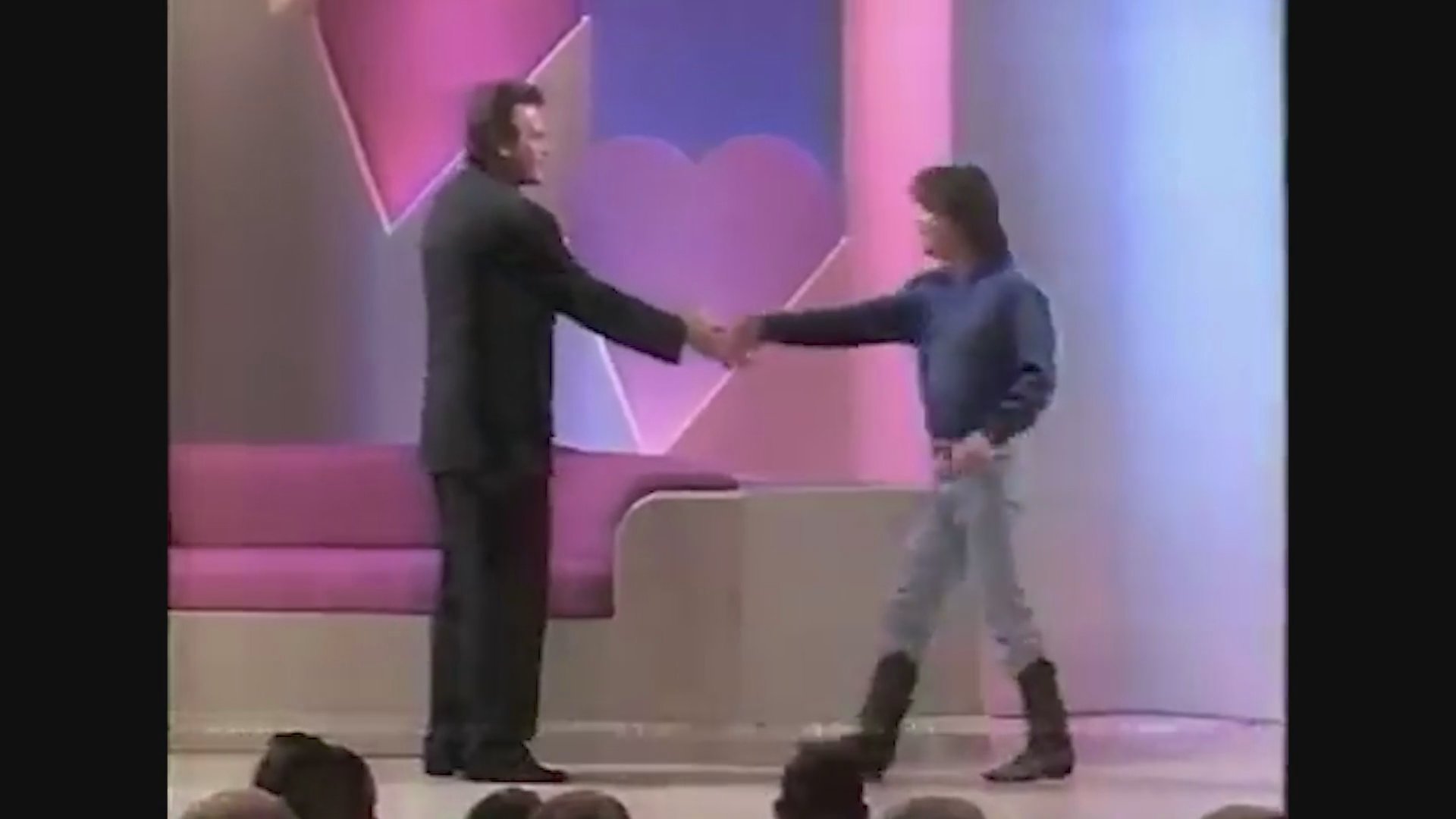 A game show host in a viking costume introduces a contestant who walks onto the brightly lit studio stage. The contestant greets the host and interacts with the audience before taking a seat.