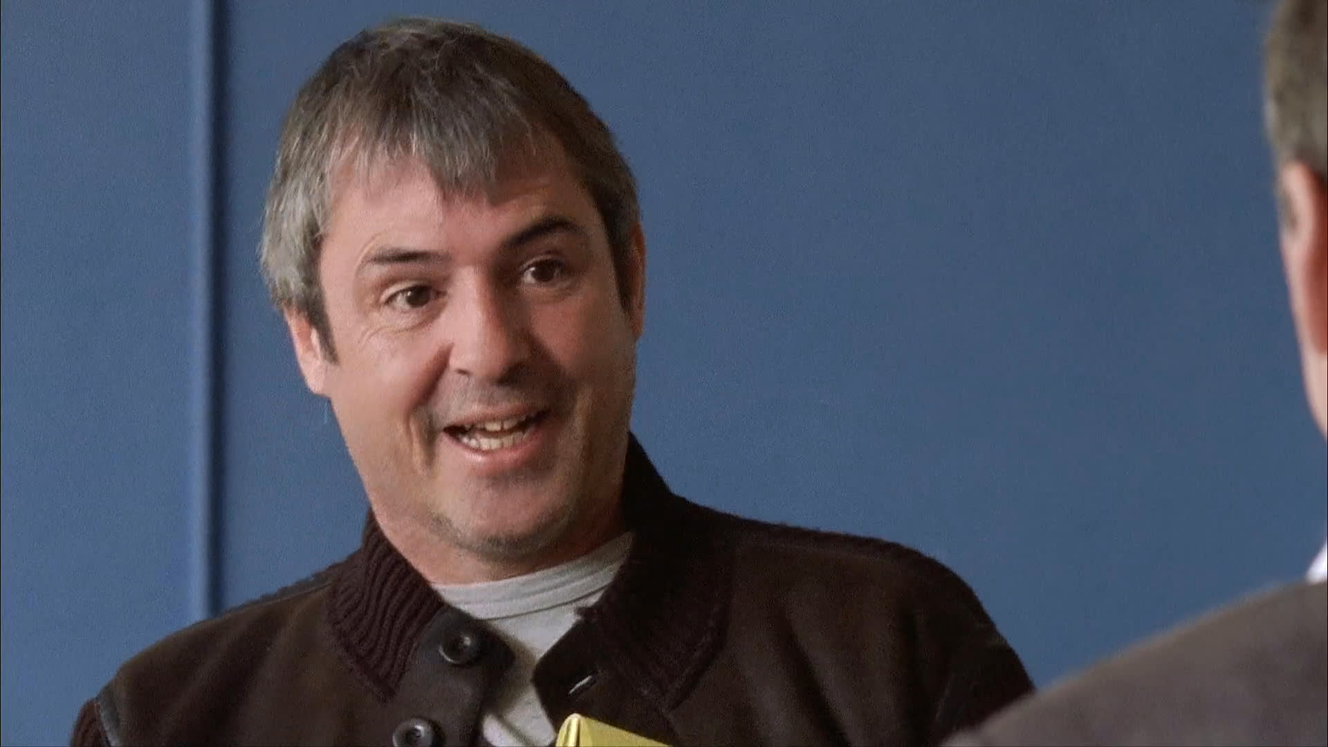 Two individuals engage in a structured, professional conversation while being filmed. One subject wears an unconventional accessory, suggesting a creative or behind-the-scenes production environment.
