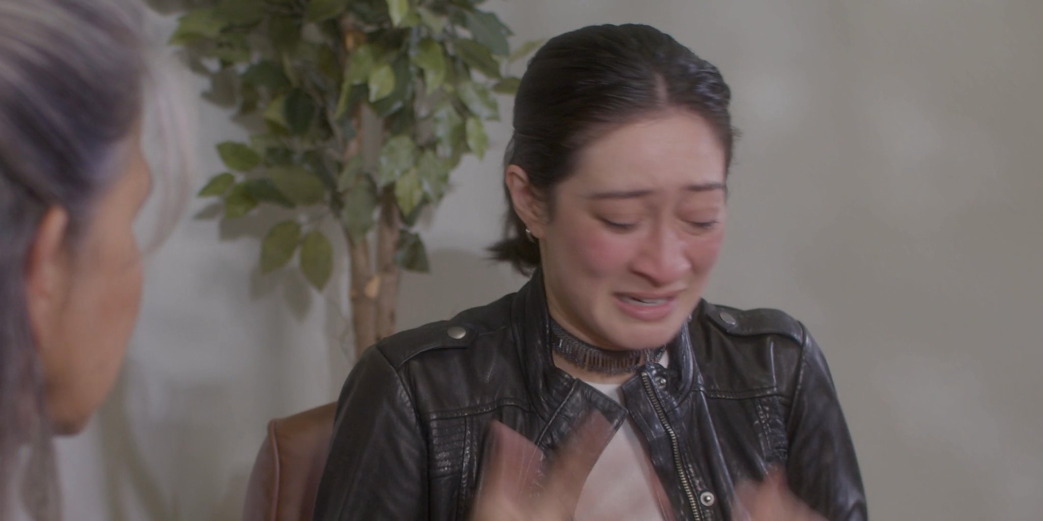 An older woman provides comfort and support to a younger woman who is visibly distressed and crying. The scene depicts a therapeutic or personal interaction centered on emotional processing and guidance.