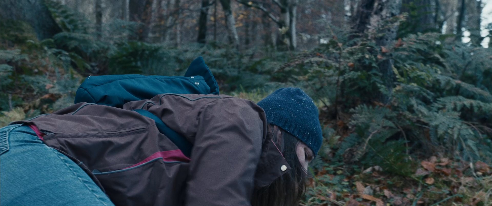 A hiker experiences a sudden fall while navigating a wooded trail, resulting in apparent injury and distress. She attempts to recover while situated on the forest floor.
