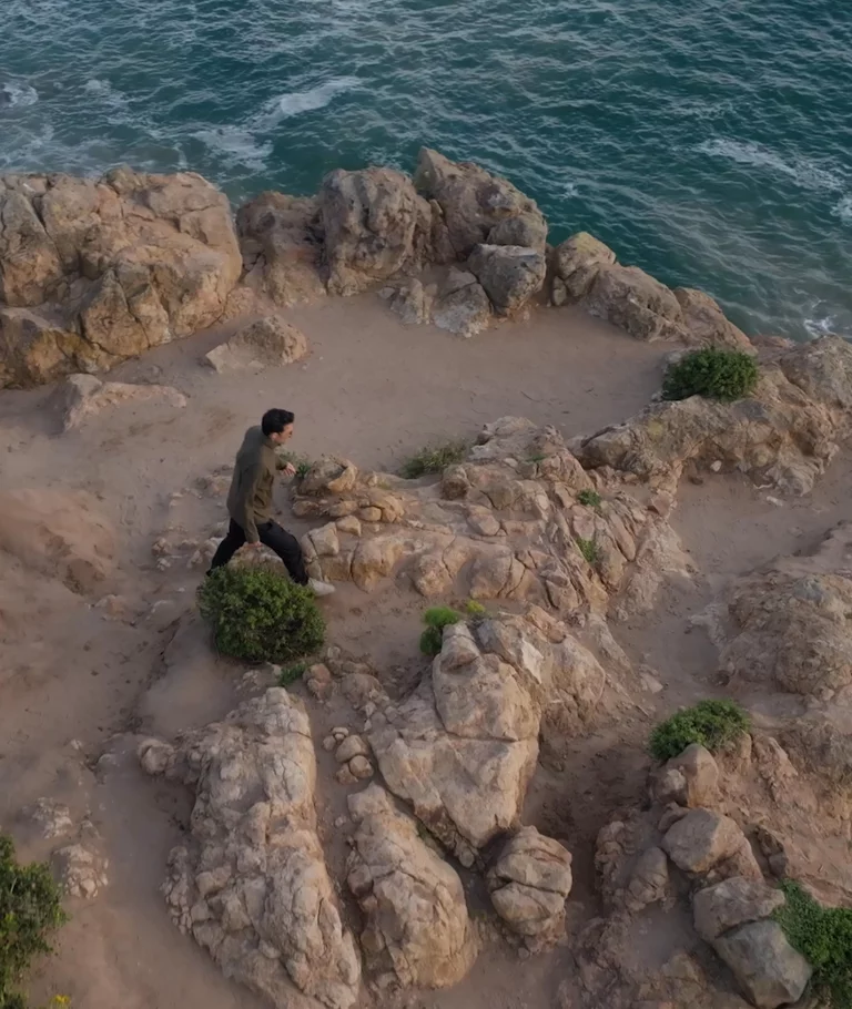 Video montage of a man in AETHER Motion clothing walking alongside ocean, in a field and standing on a large boulder overlooking the ocean