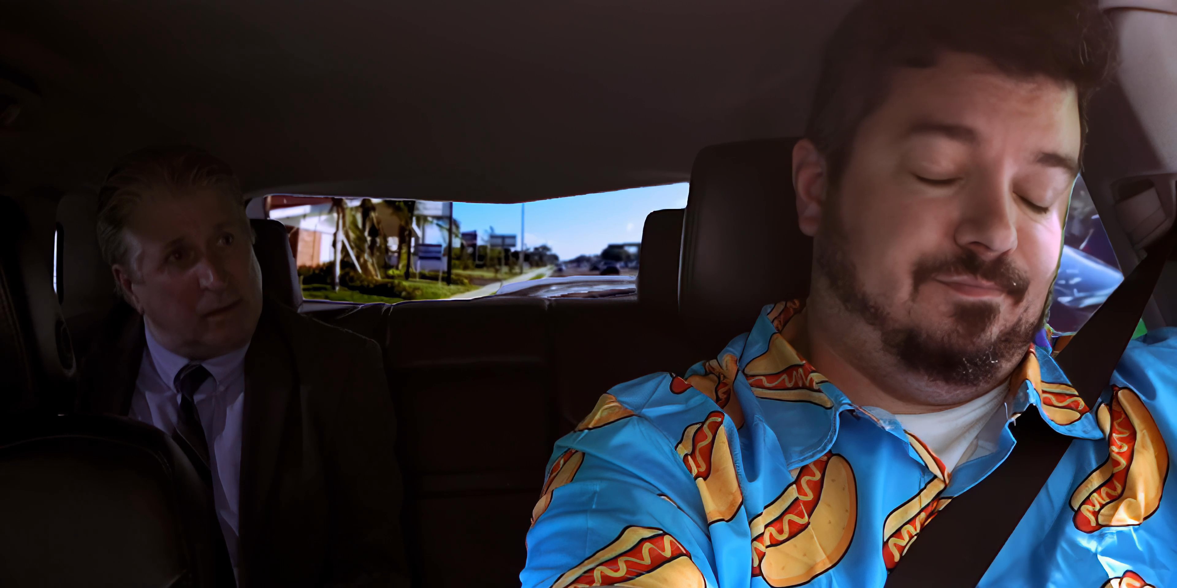 Two men ride in the backseat of a vehicle, observing the passing scenery while engaged in a conversation.