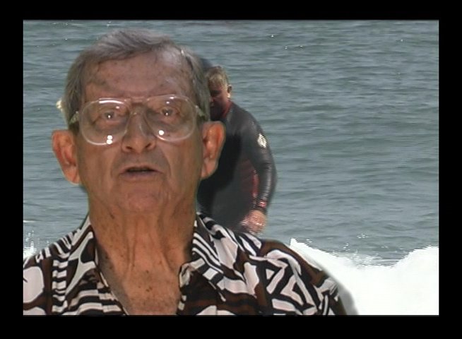 An older man in a patterned shirt provides a testimonial while archival footage of a man in a wetsuit surfing ocean waves is superimposed over the background.
