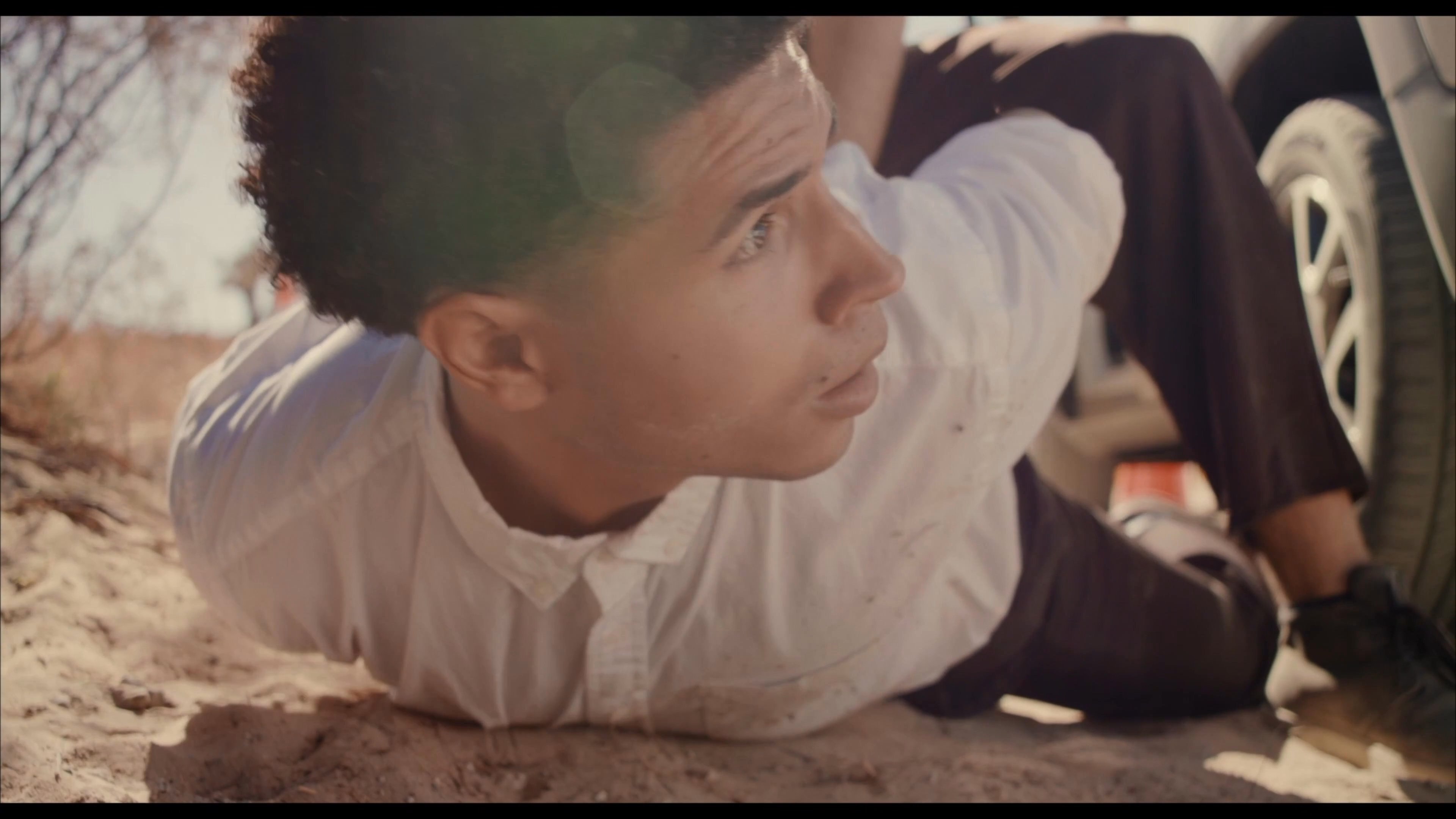 An agent inspects a bag of narcotics recovered during an arrest in a remote desert location. The scene transitions to a flashback depicting the initial apprehension of a suspect on the ground.