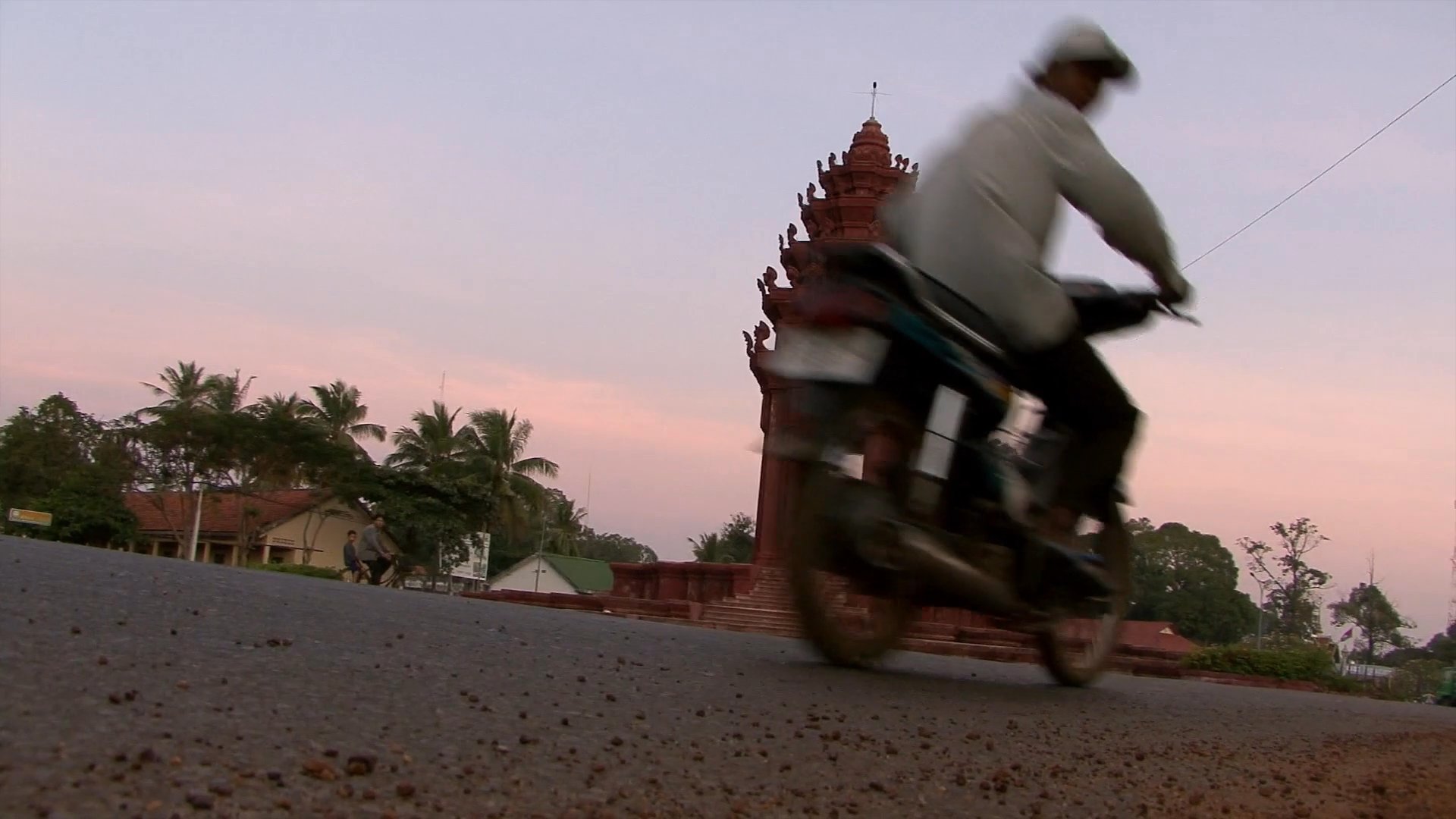 The footage contrasts dense urban traffic in a busy city center with serene, traditional rural life in Baribo, Cambodia, featuring ox-carts and local commuters.