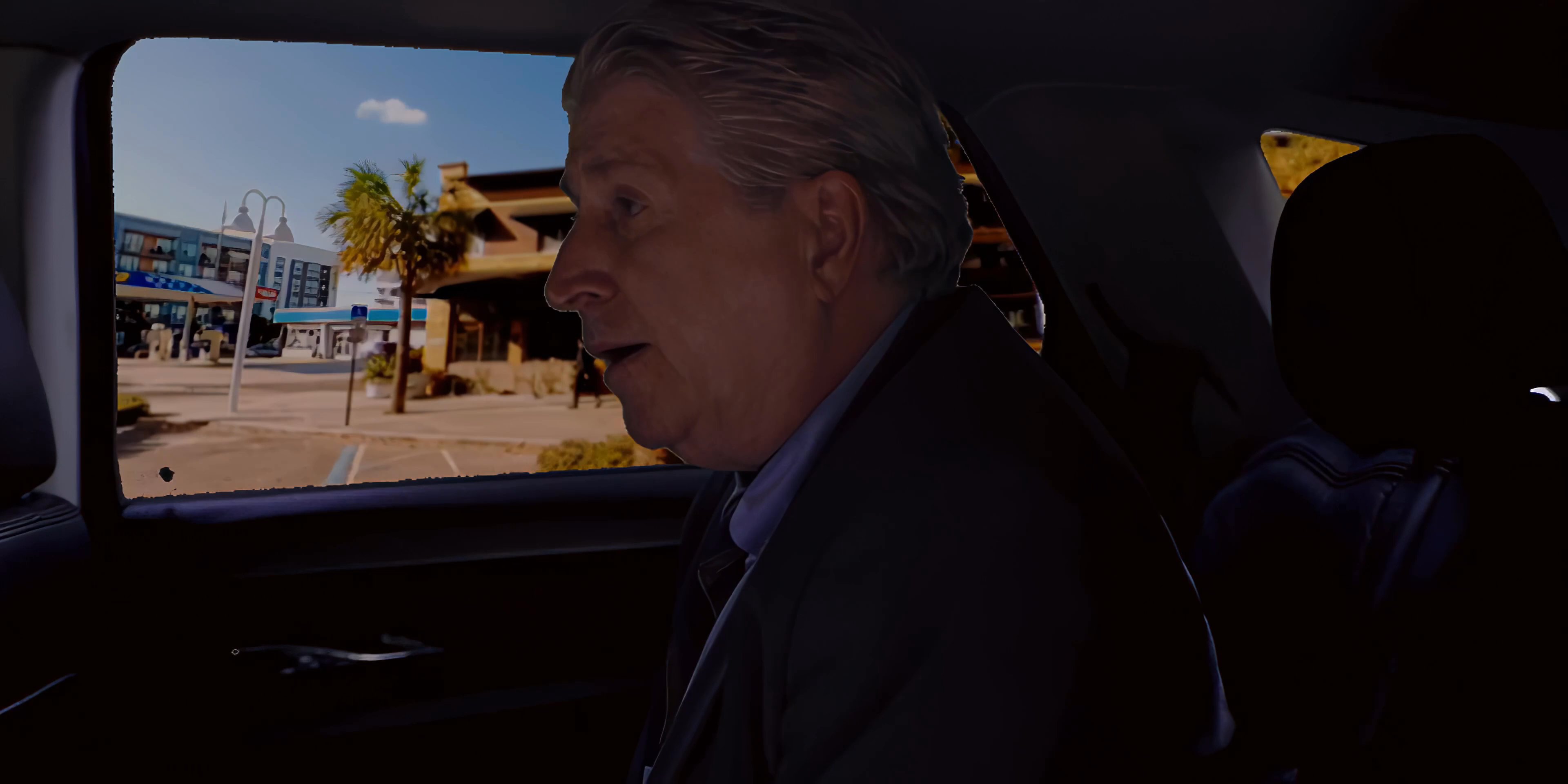 Two men engage in a serious discussion while traveling as passengers in a car, with one individual holding a stack of currency.