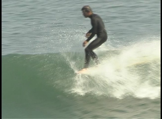 A surfer wearing a wetsuit skillfully maneuvers a surfboard across the face of a rolling ocean wave. The individual maintains balance and control while gliding through the surf.