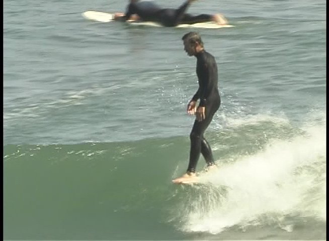 A man in a wetsuit skillfully maneuvers his surfboard across the face of a rolling ocean wave. He maintains balance and control while riding the surf toward the shore.