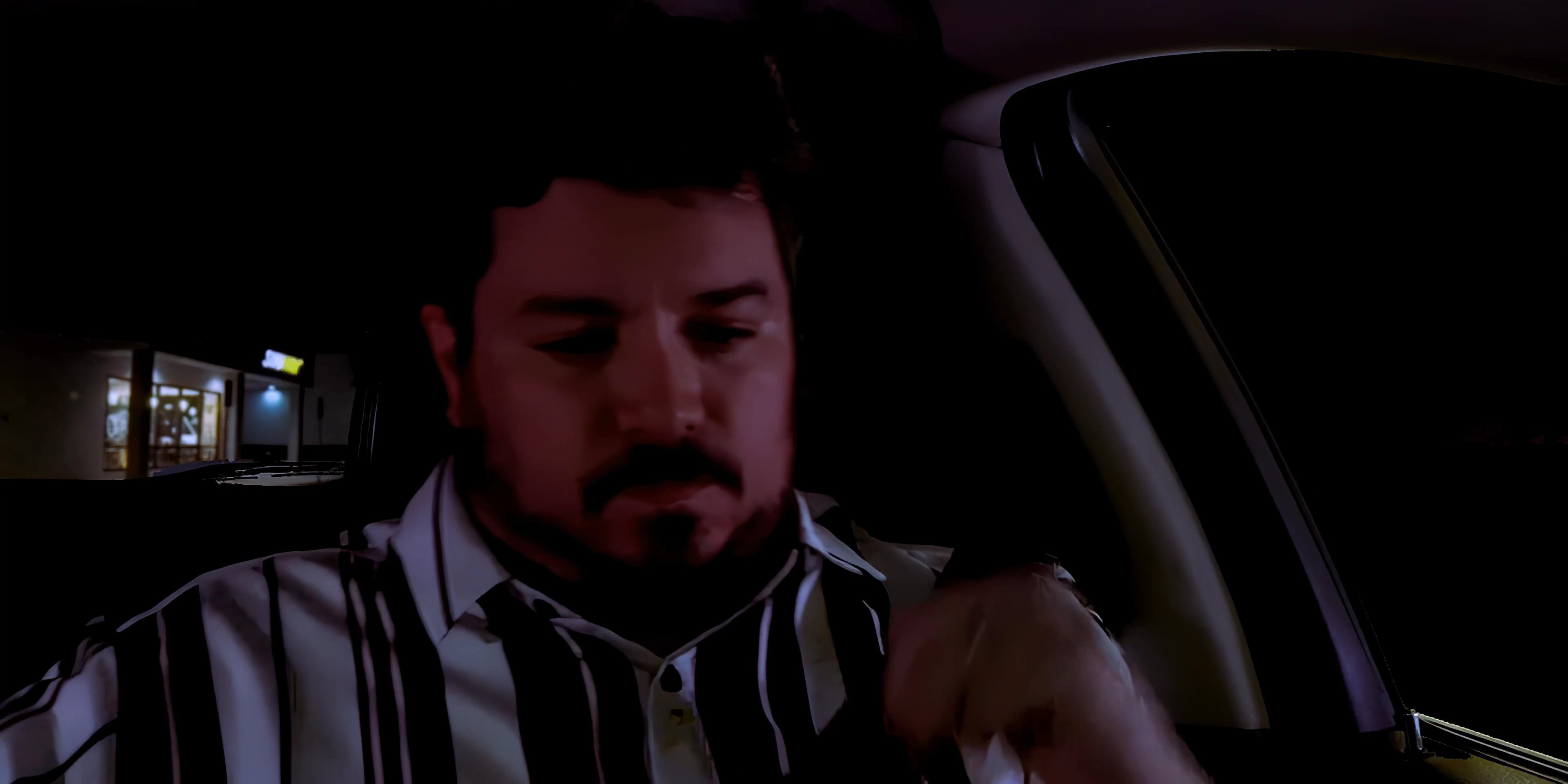 A man approaches his car in a parking lot during nighttime hours, enters the driver's seat, and prepares to depart. The sequence highlights the quiet transition from exterior movement to interior focus as he settles into the vehicle.