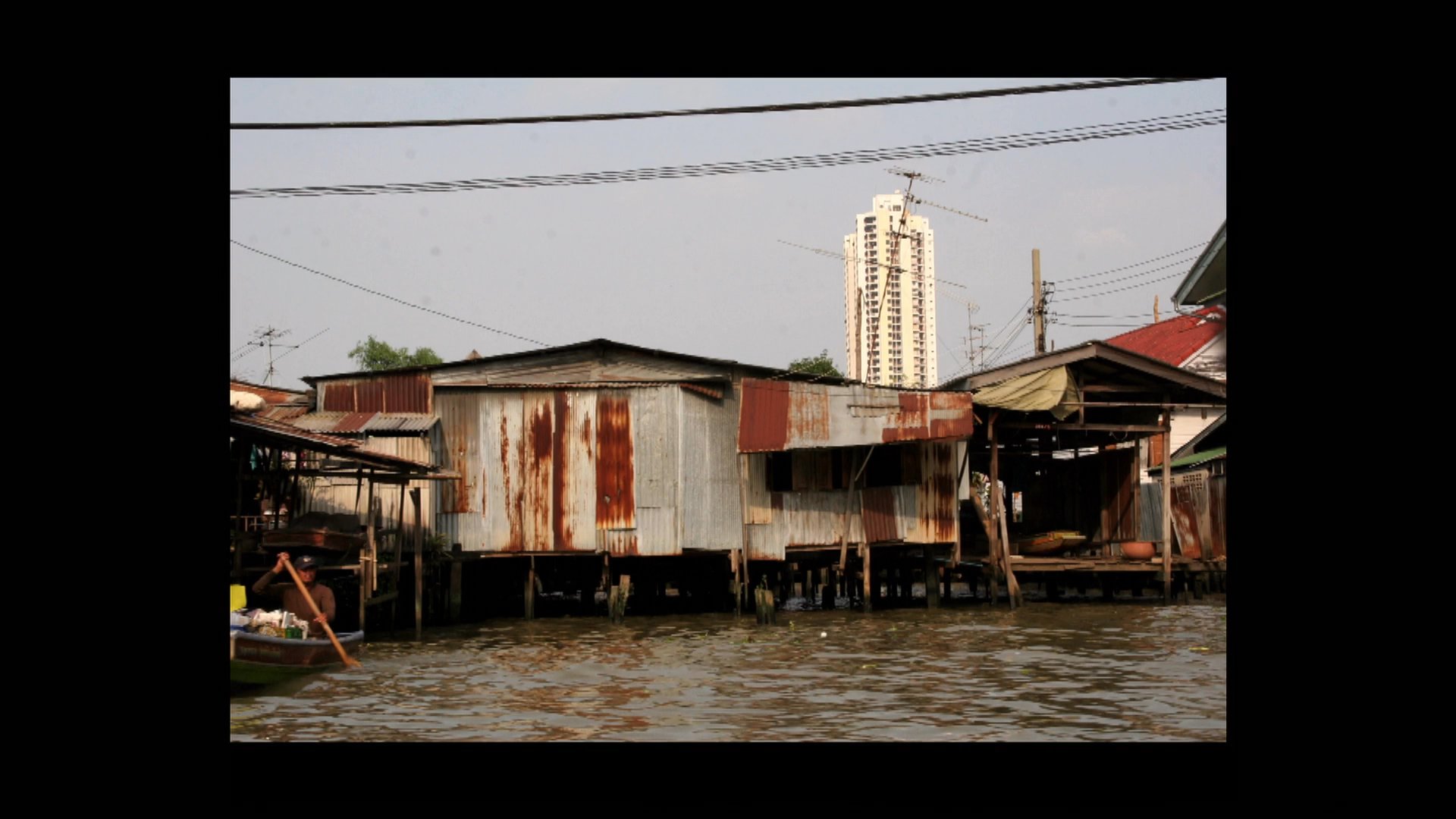 The sequence captures the contrast between Bangkok's bustling river transport, including traditional long-tail boats and passenger ferries, and the city's modern road infrastructure. Viewers observe daily life along the waterfront transitioning to transit scenes and expansive city views.