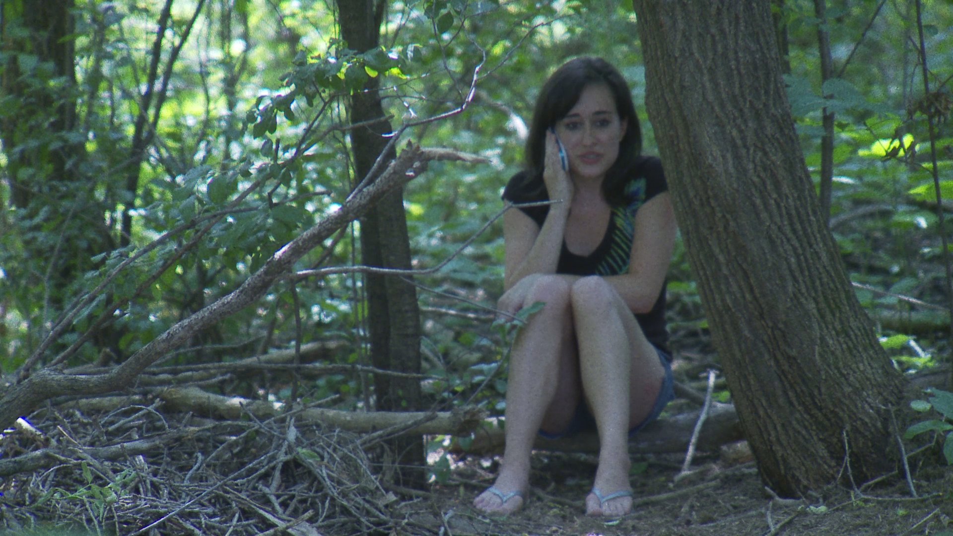 Two individuals engage in mobile phone conversations while spending time in a wooded park setting with a golden retriever.