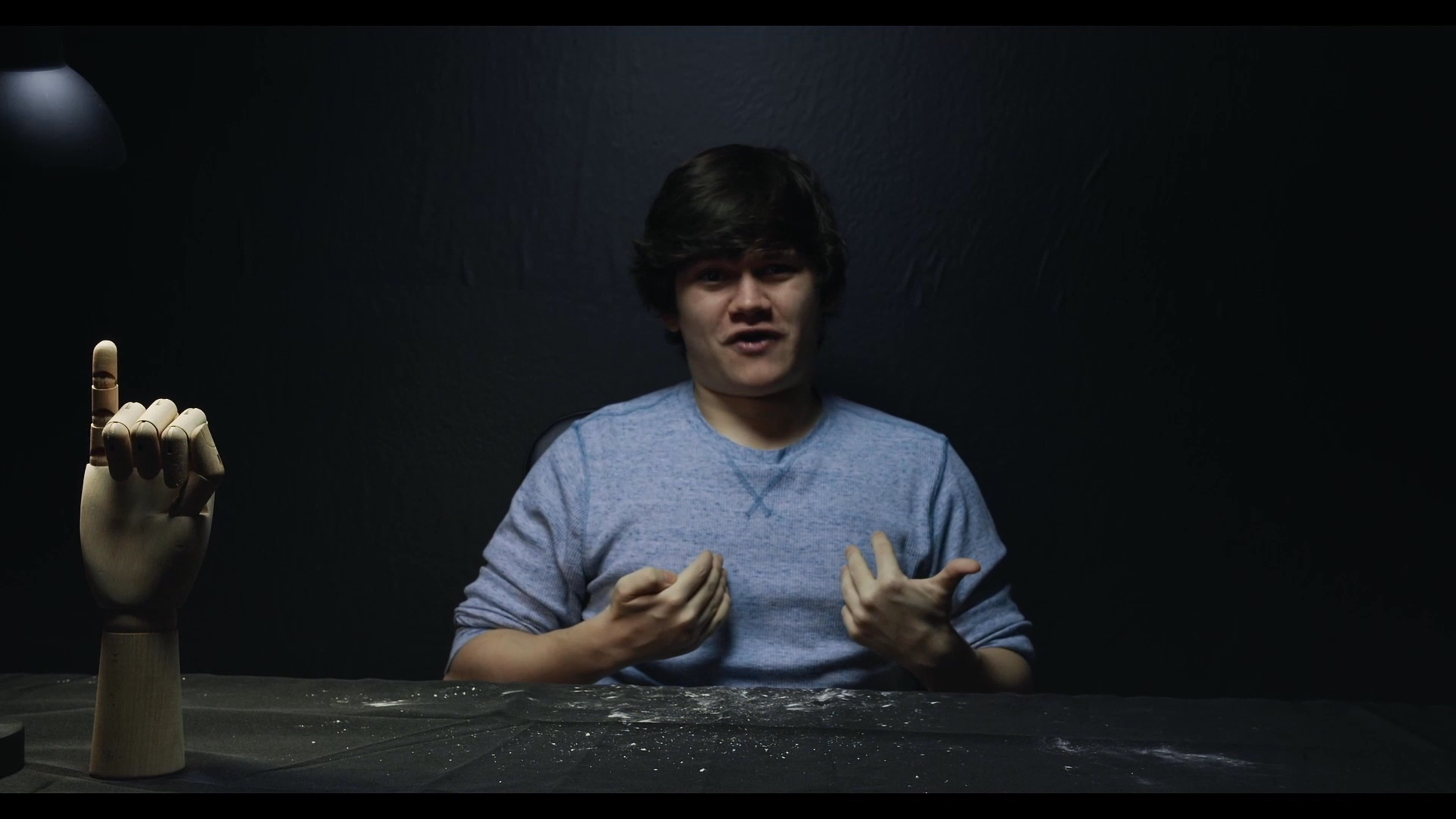 An actor performs an intense emotional scene in a dark studio while being observed by two evaluators. The sequence highlights varied physical expressions and dramatic delivery.