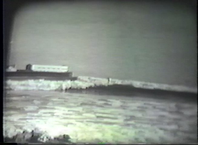 A surfer runs into the ocean with a board and navigates waves near a coastal pier. The footage captures classic surfing activity in a serene marine environment.