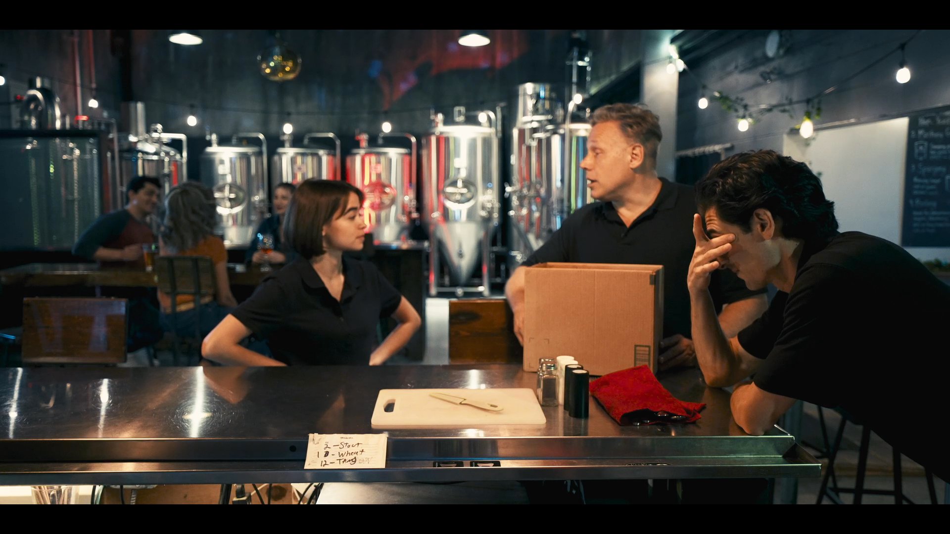 Three professionals engage in a structured discussion across a bar counter in a brewery, focusing on a cardboard box as a key point of their interaction.