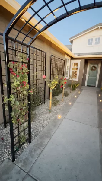 decorative iron garden arbor with a grid trellis design, climbing vines, and young rose bushes.