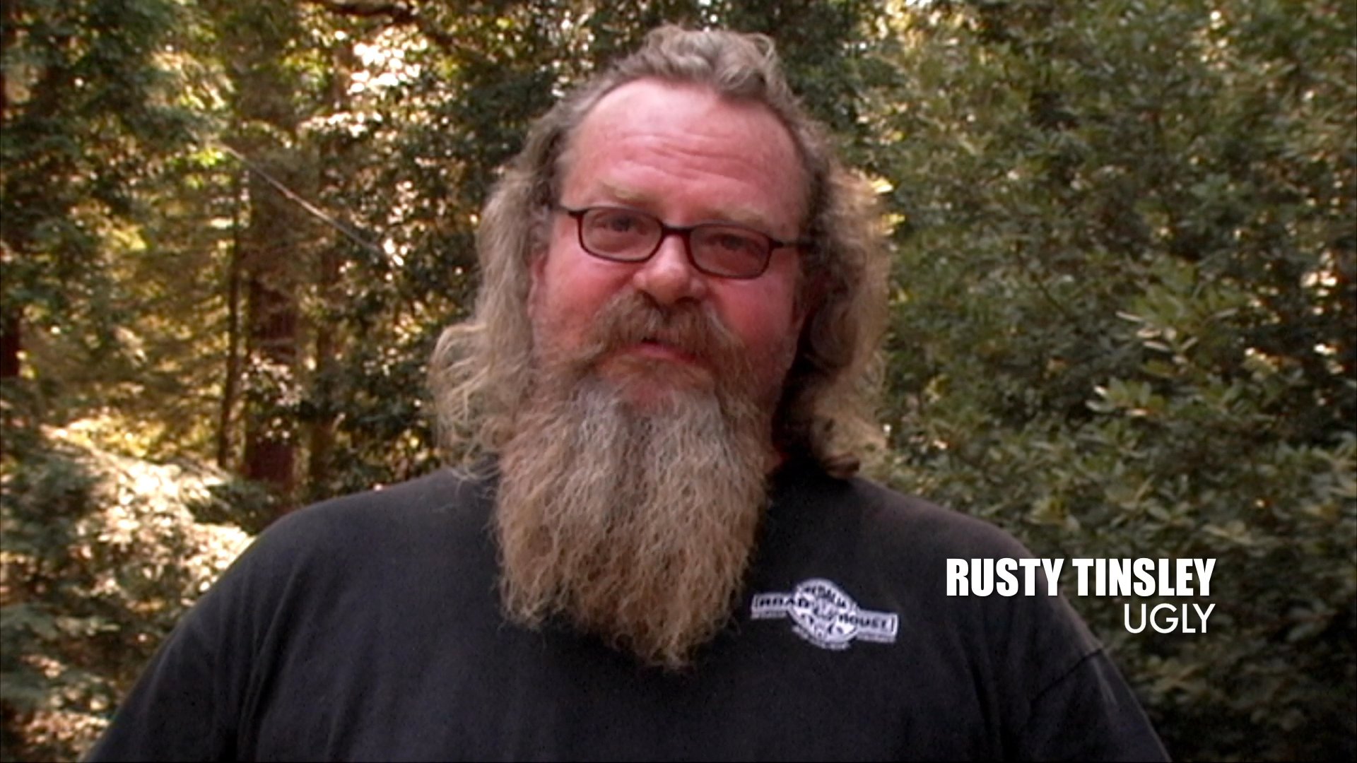 Rusty Tinsley provides a direct-to-camera testimonial against a wooded background, recounting personal experiences in a documentary-style setting.