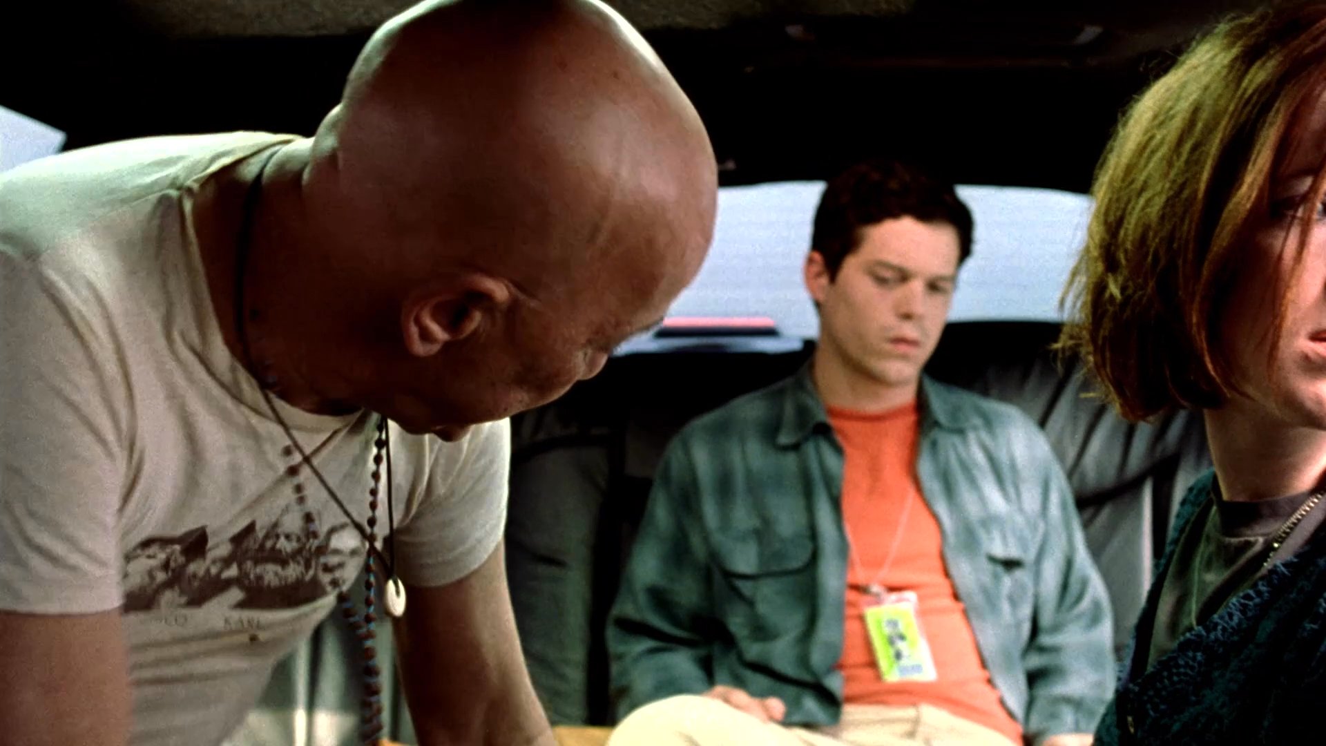 An intense encounter unfolds inside a moving limousine as a man aggressively confronts two passengers before handing over a security badge. The atmosphere remains charged with unspoken threats and palpable anxiety during the transit.