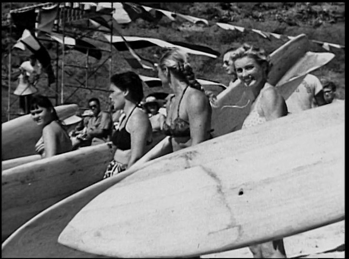 Surfers navigate coastal waves before transition to a beach gathering and a surf-themed vehicle driving along a rural road. The imagery captures the classic lifestyle and transport associated with mid-century surf culture.