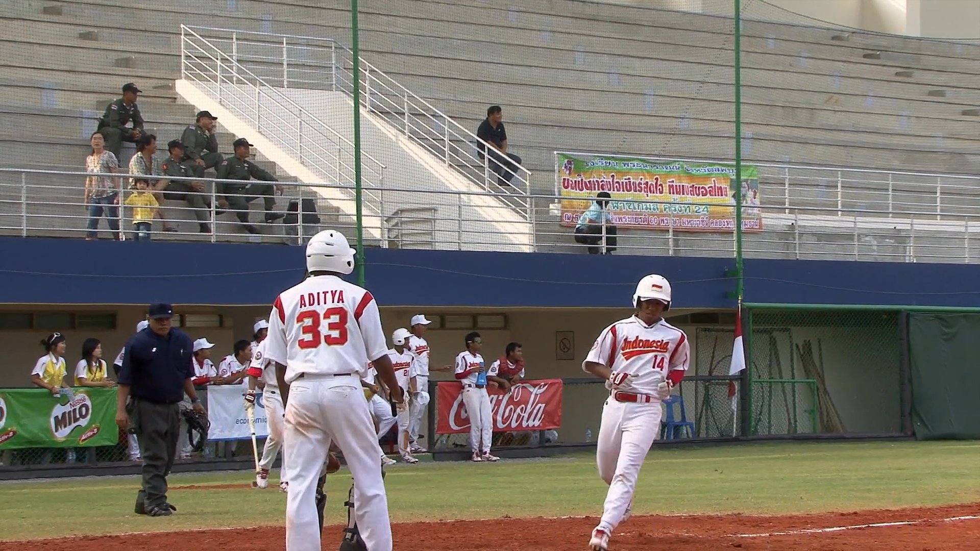 A baseball player hits a home run and rounds the bases as the scoreboard reflects the game progress between Indonesia and Cambodia. The sequence captures the swing, the run, and the subsequent pitcher maneuvers on the field.