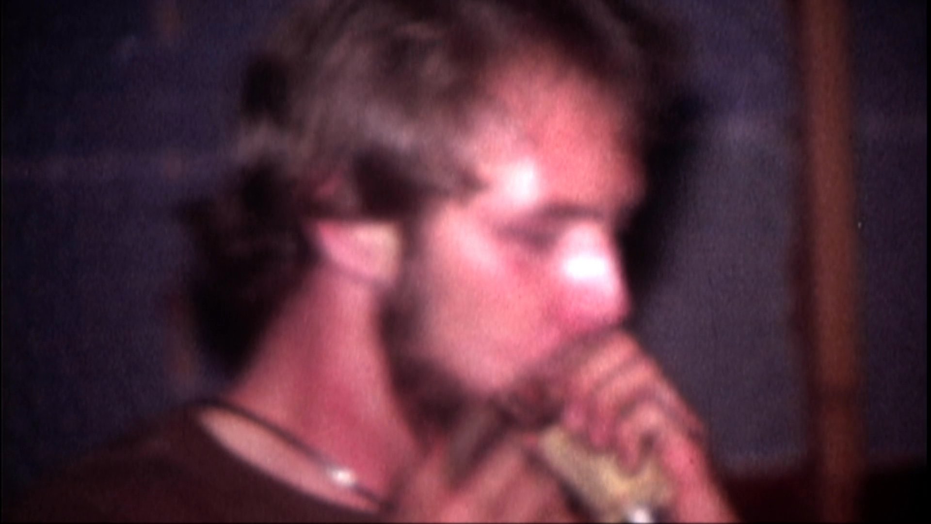 A musician plays a harmonica in a dimly lit setting before transitioning to an interview with a bearded man and a live performance by a country band on stage.