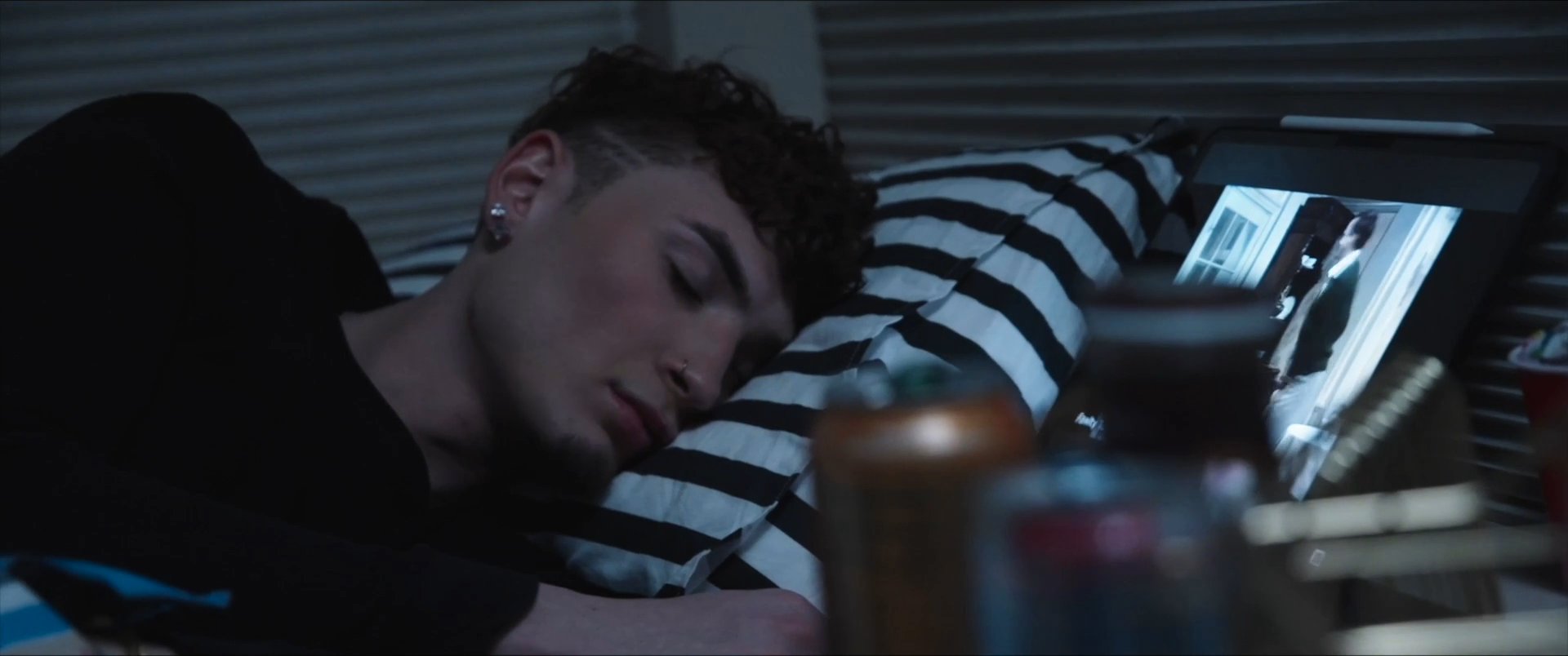 An audience applauds in a decorated hall before the scene shifts to an individual resting alone in a dark room. The narrative concludes with the person walking through their home near a pride flag.