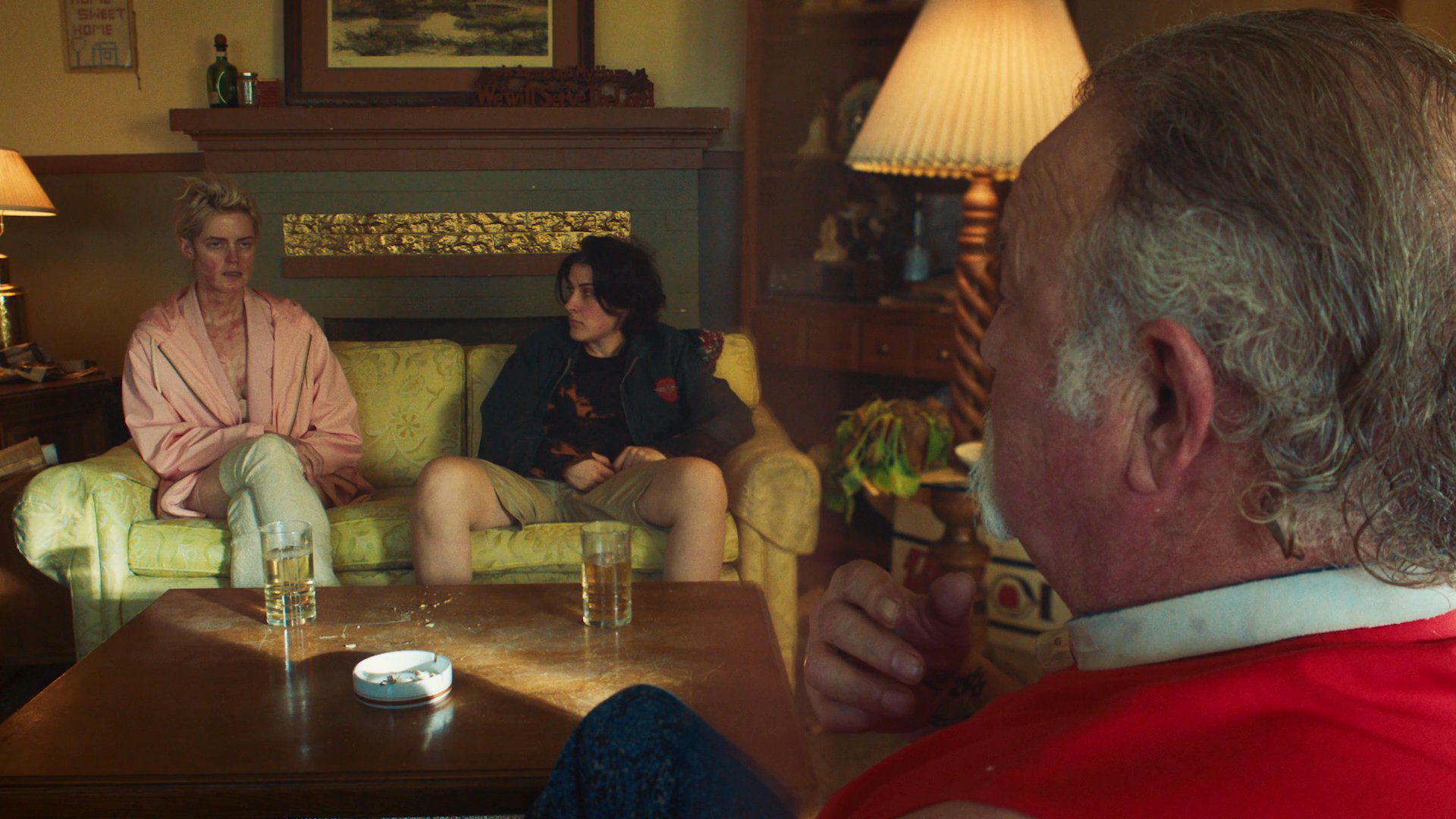 An older man sits across from two younger people in a living room, engaging in an intense, emotionally charged conversation.