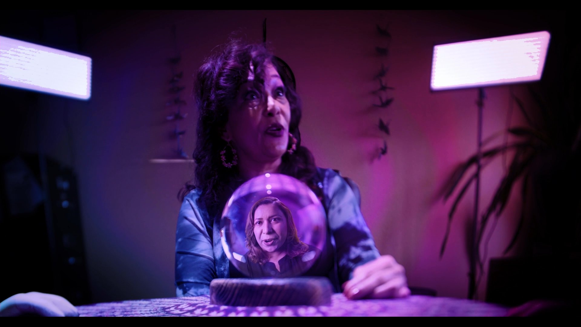 A psychic medium performs a mystical reading with a crystal ball while interacting with clients in a dimly lit, atmospheric setting. The sequence captures a professional portrayal of spiritual consultation and supernatural communication.