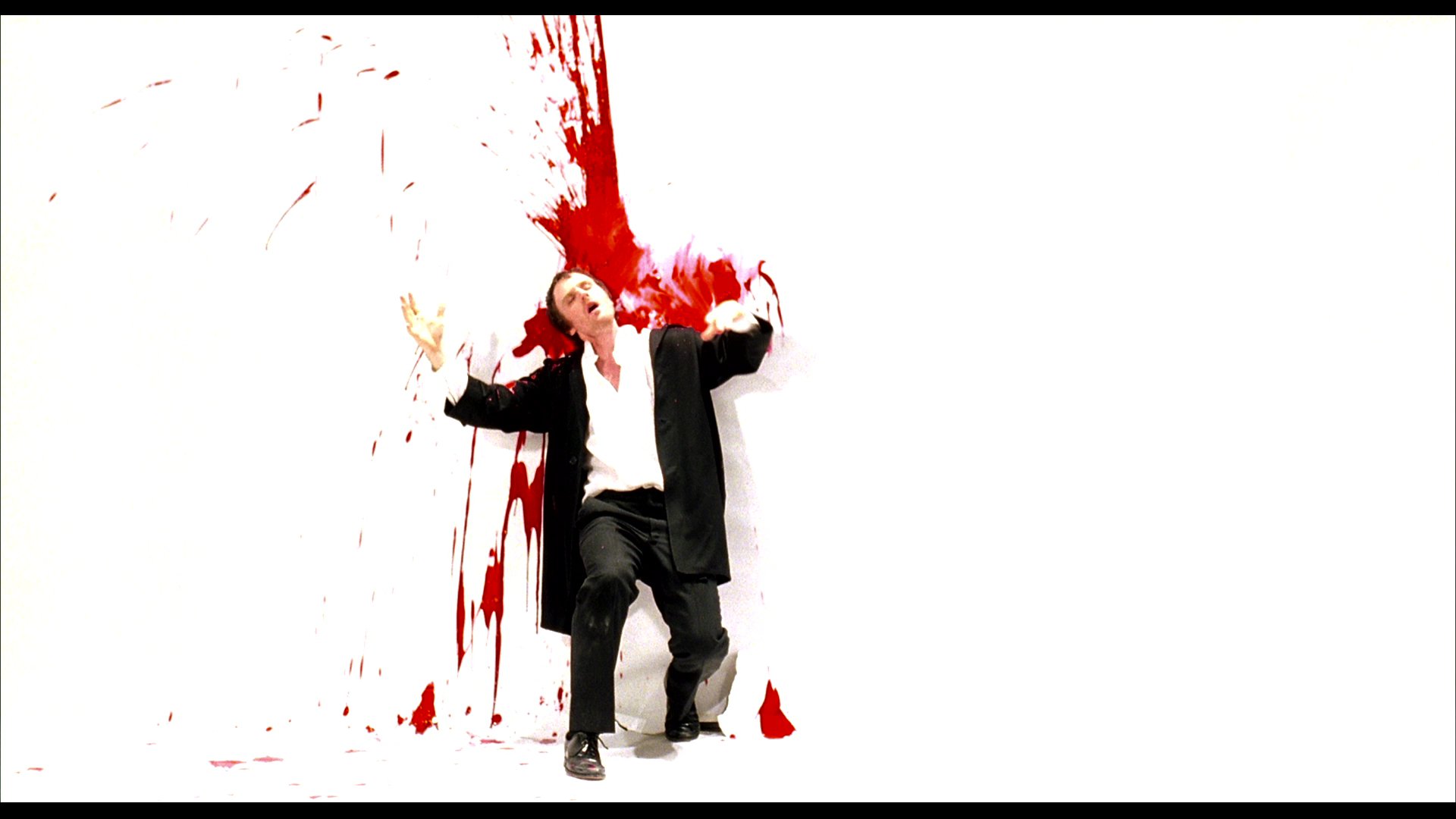 A man in a suit performs a sequence of movements against a white backdrop as red paint splashes behind him, concluding with the end credits.