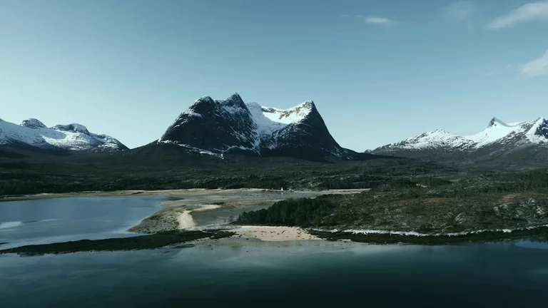 Drone video of remote shoreline in Northern Norway with snow-capped mountains in the background
