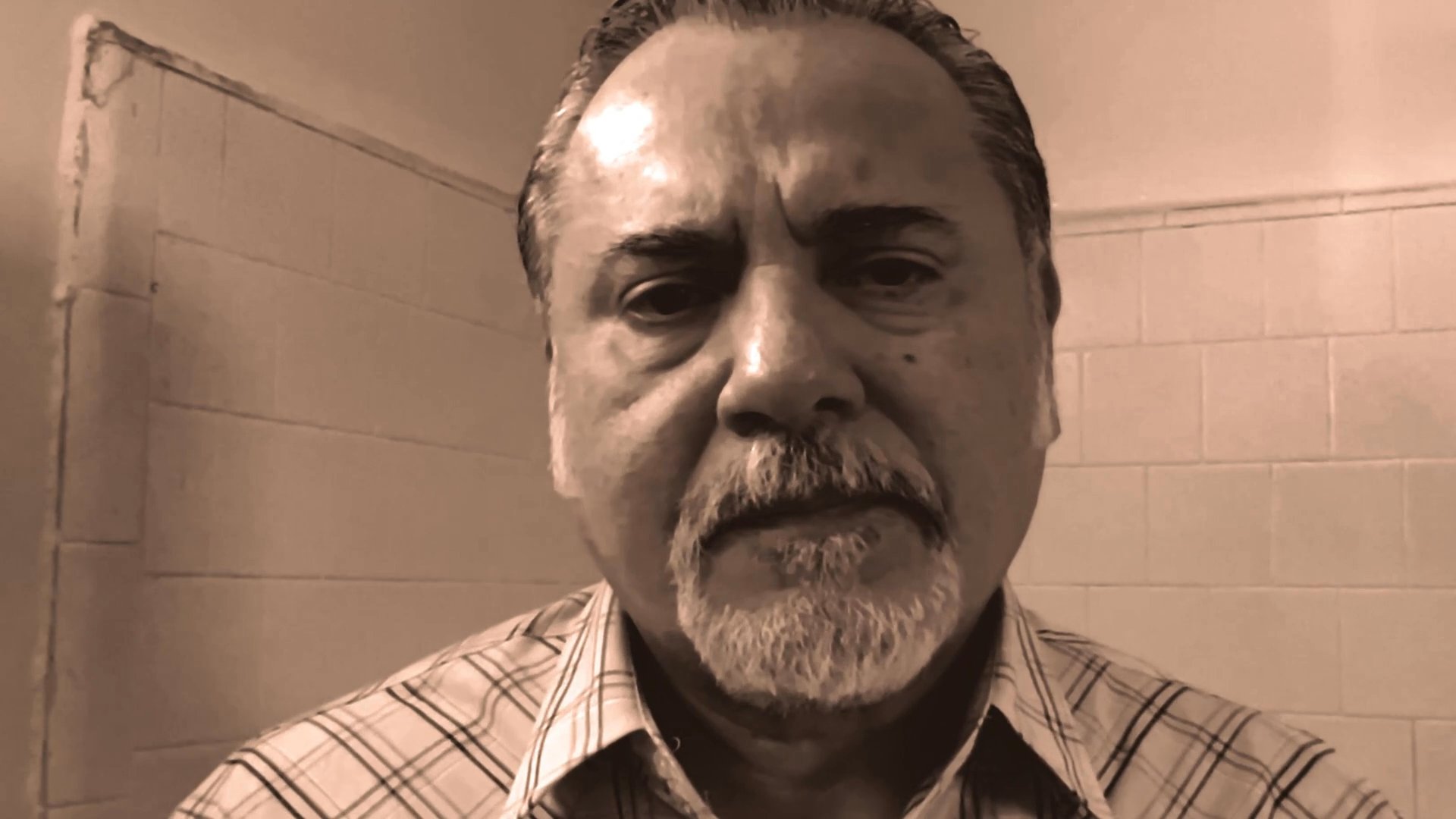 A man speaks directly to the camera in a close-up portrait, conveying a serious message through his facial expressions and verbal delivery.
