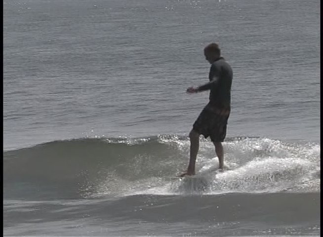Surfers in wetsuits skillfully navigate various ocean waves along the coastline. The footage captures multiple individuals engaging in surfing activities across different water conditions.