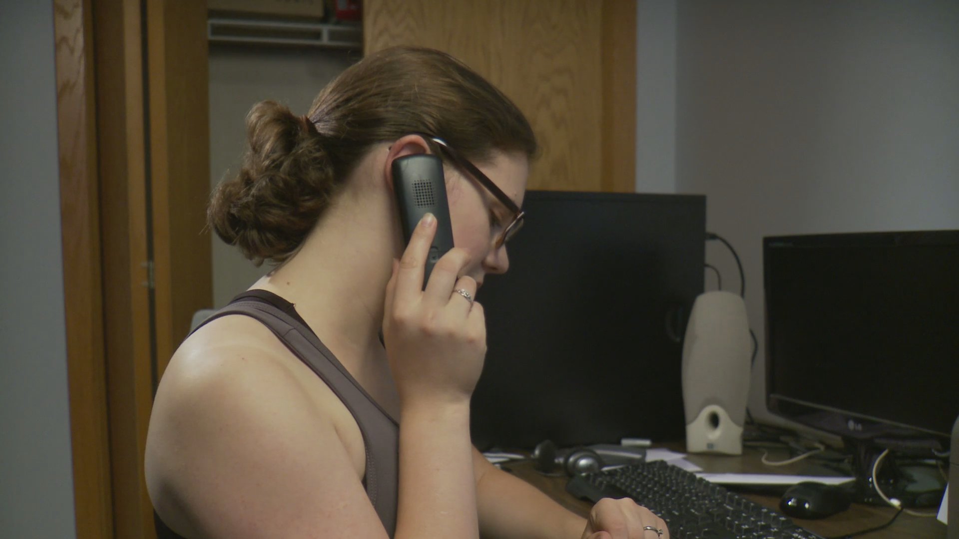 An older man and a younger woman engage in separate, private phone conversations within an office setting. The individuals appear focused and contemplative while communicating over the phone.